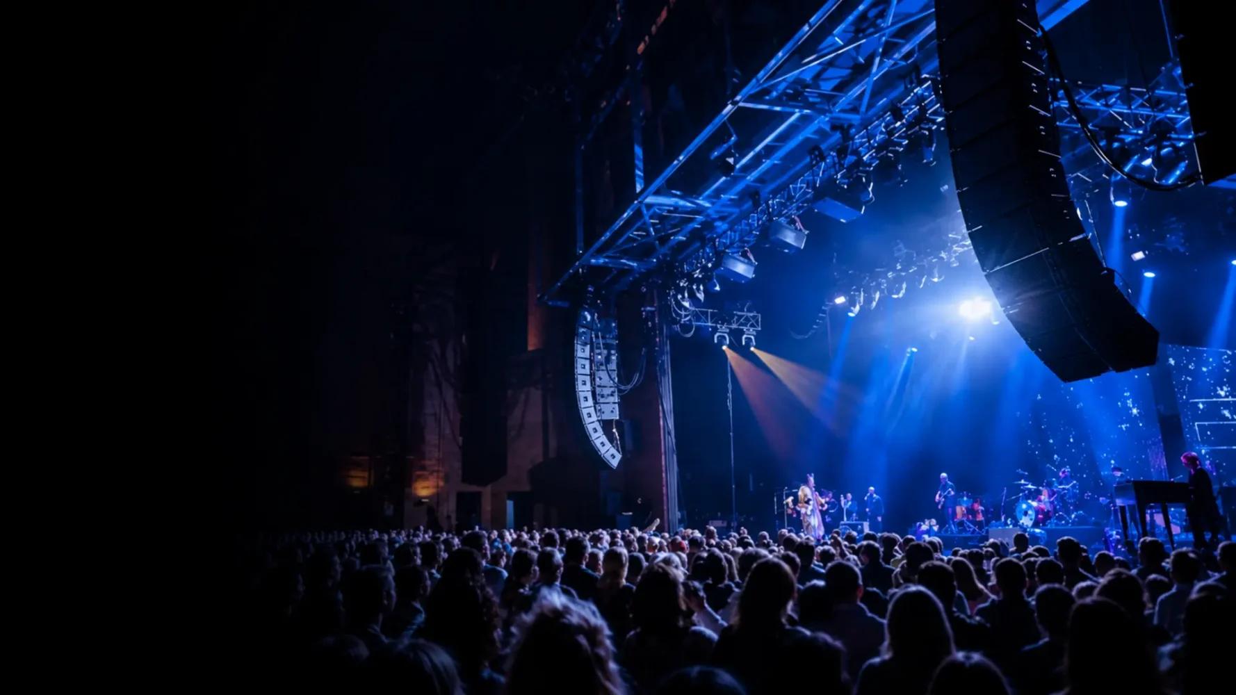Audio hire setup with suspended line-array speakers above a blue-lit concert stage and audience.