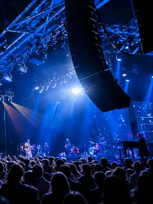 Large suspended line-array speaker beside a live concert stage illuminated in blue.