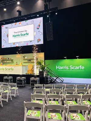Overhead event screen showing The Kitchen by Harris Scarfe above a branded stage.