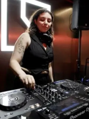 DJ wearing headphones around her neck and operating professional DJ equipment.
