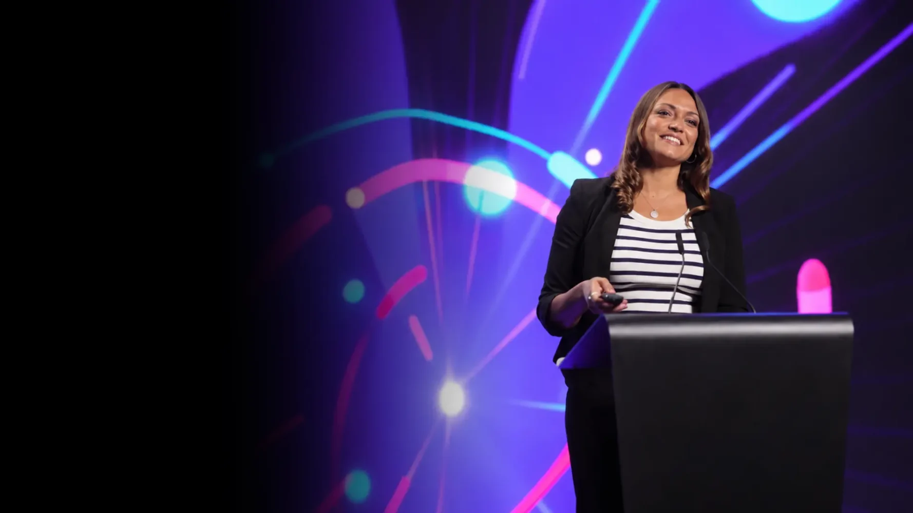 Conference presenter speaking at a black lectern against a purple, cyan and magenta stage backdrop.