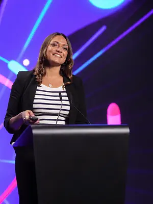 Presenter holding a presentation remote behind a lectern with microphones.