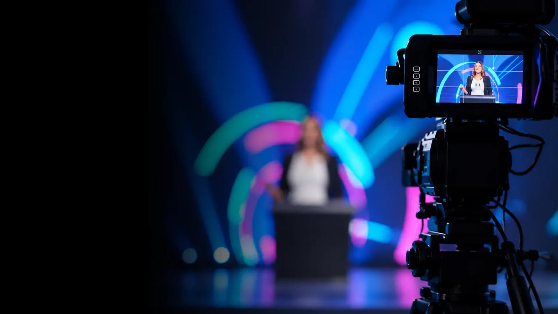 Hybrid live streaming production with a professional camera filming a presenter on a blue-lit corporate stage.
