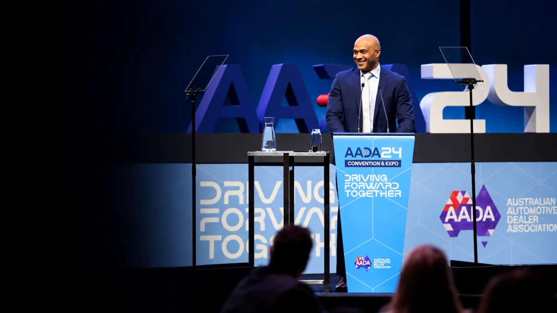 Lectern hire setup with a branded blue podium, twin microphones and teleprompters on a conference stage.
