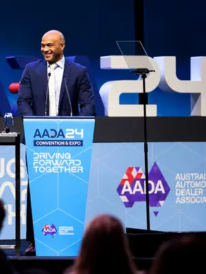 Conference presenter standing behind a blue branded lectern with two microphones.