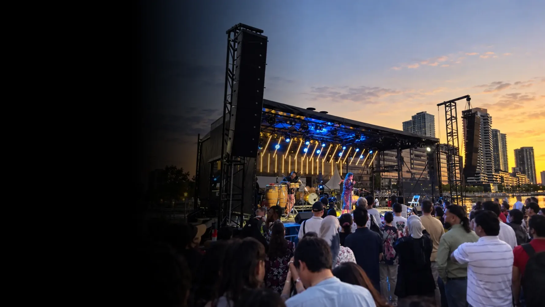 Mobile stage trailer hire with a covered performance stage, concert lighting and speaker towers at an outdoor event.