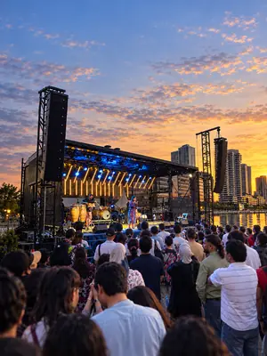 Musicians performing on a covered mobile stage before an outdoor crowd at sunset.