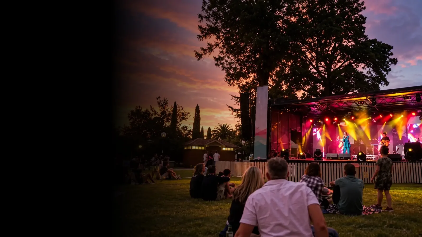Outdoor event production with a live stage, professional lighting and guests seated on the lawn at sunset.
