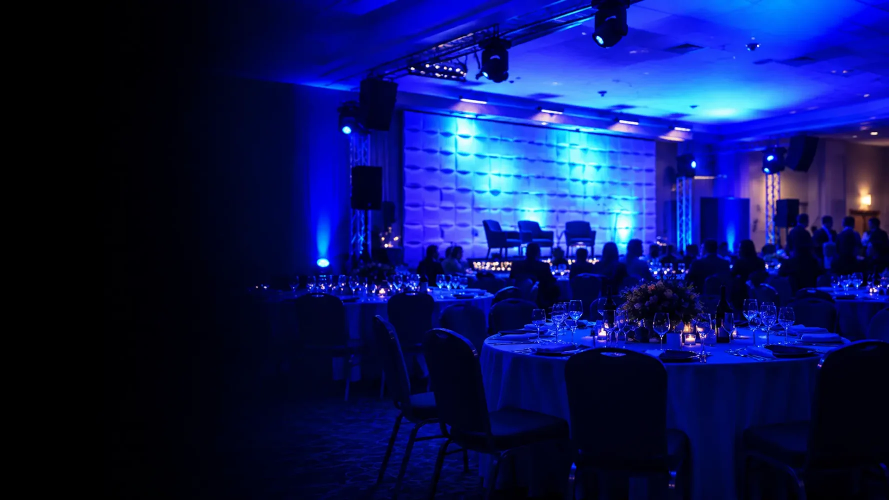 Room lighting hire with blue and cyan uplighting illuminating a banquet room and presentation stage.