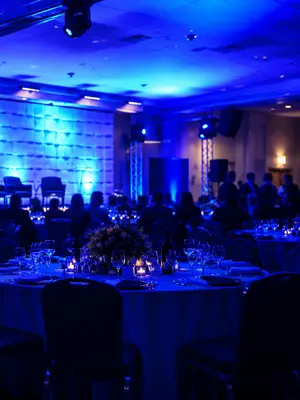 Blue event lighting across banquet tables, chairs and a textured stage backdrop.