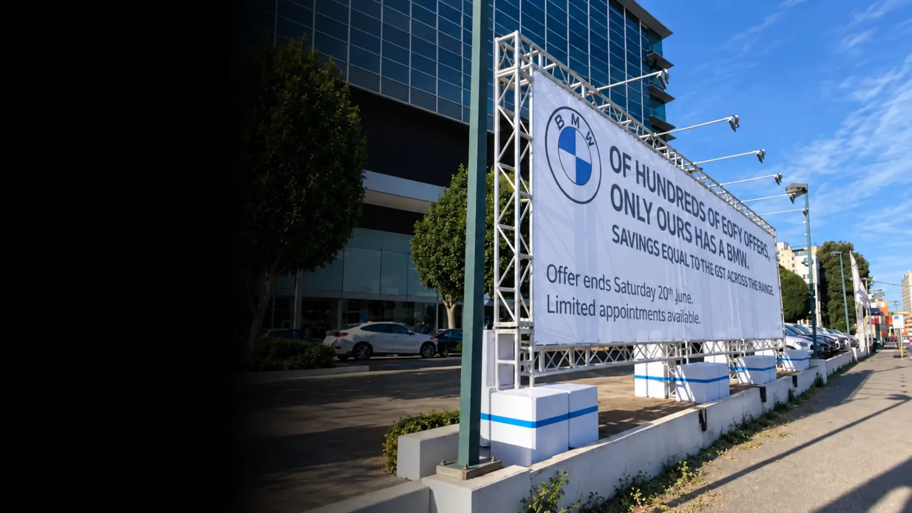 Large outdoor branded banner mounted on a silver truss frame with overhead lights and weighted bases.