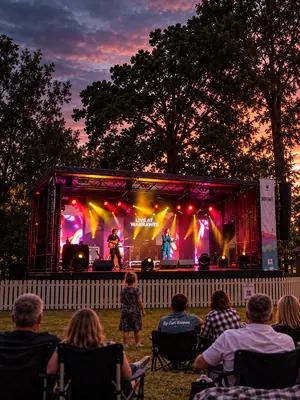 Covered outdoor stage with a singer and guitarist performing under yellow and magenta lights.