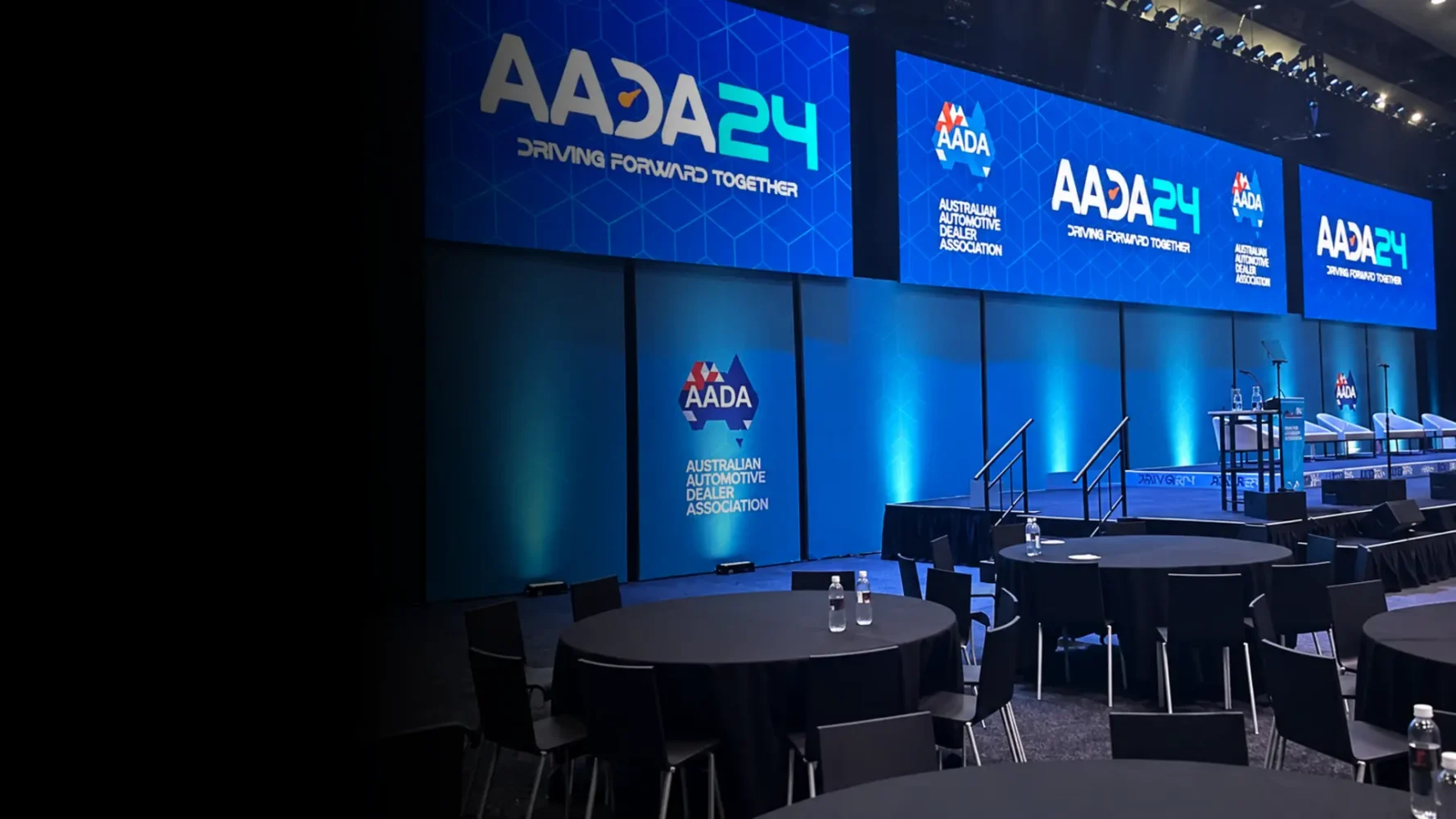 Vision hire setup with large LED screens displaying AADA24 branding above a blue-lit conference stage.