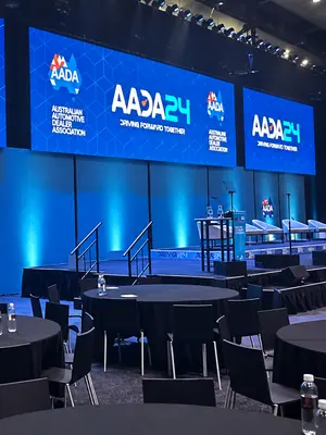 Conference LED screens above a presentation stage with a lectern and seating.