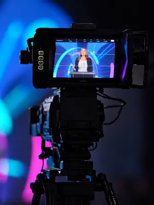 Camera monitor showing a presenter at a lectern during a live event.